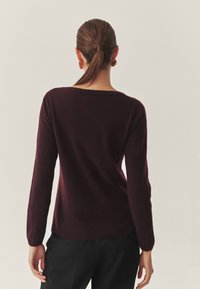 Burgundijas adīta džemperis ar garām piedurknēm un plašu kakla izgriezumu, ar ribotām aprocēm un apakšmalu, mīksta tekstūra un pieguļošs siluets.