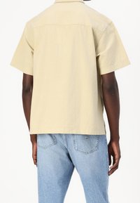 Korte mouwen shirt van lichtbeige stof, met een ontspannen pasvorm en klassieke kraag. Gecombineerd met lichtblauwe denim jeans.