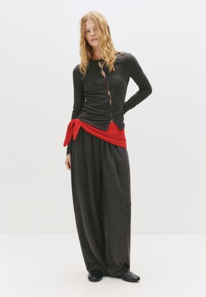 Zwarte lange mouwen cardigan met knopen, gecombineerd met losse grijze broek, accentueert met een rode tailleband. Beide kledingstukken hebben een zachte textuur.