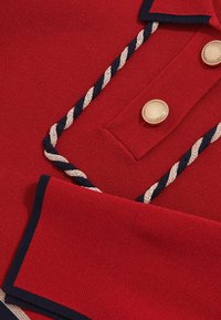 Polo rosso con tessuto testurizzato, caratterizzato da un collo blu navy, dettagli in corda crema e bottoni rotondi dorati.