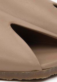 Beige leather sandal featuring cut-out design and smooth texture. The sole is slightly transparent with a rounded edge and minimal detailing.