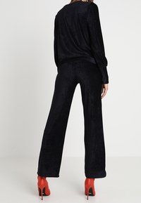 Svart, strukturerad tvådelad outfit som består av en lös topp med långa ärmar och vida byxor. Bärs med röda högklackade skor.