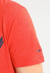 Czerwona bawełniana koszulka z krótkim rękawem. Posiada ciemnoniebieską grafikę na piersi oraz małą łatkę z logo na lewym rękawie.