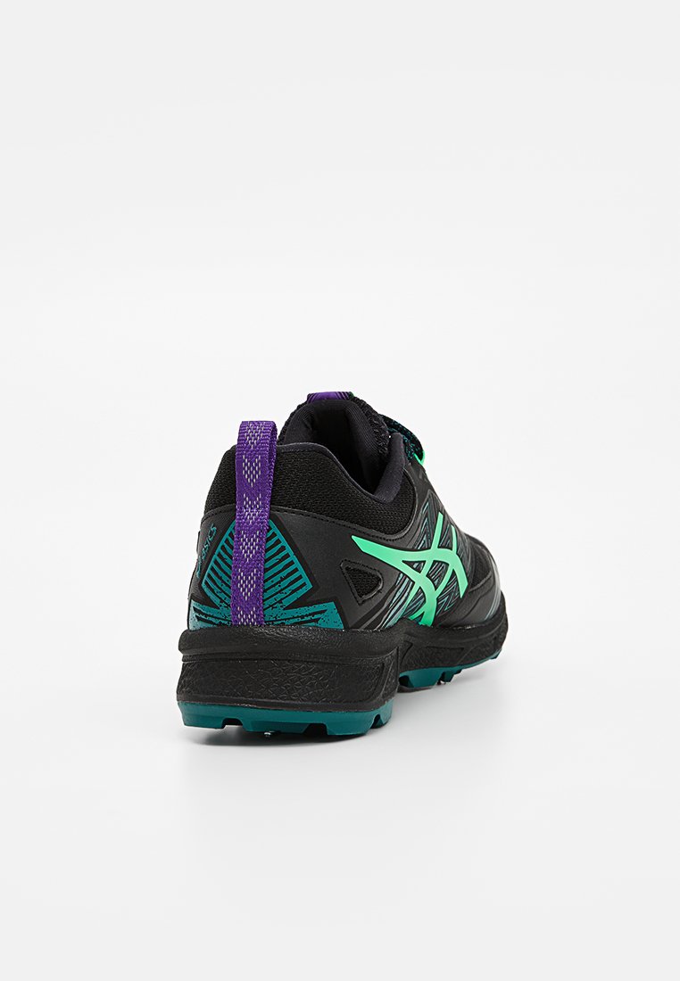 Zapatilla deportiva negra con acentos verdes, superficie texturizada y una pestaña en el talón de color púrpura; cuenta con un diseño estampado en el costado y una suela resistente.