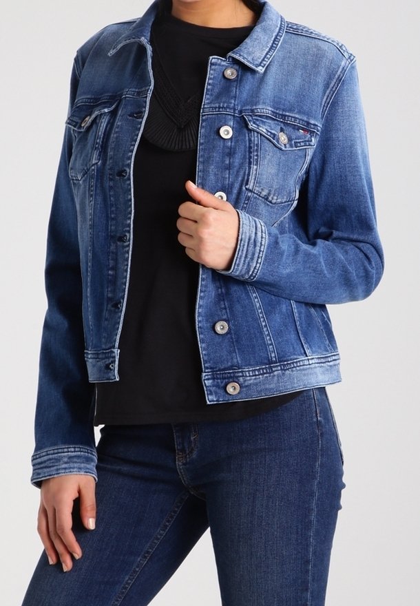 Jeansjacka i medelblått med klassisk krage, framknappning och bröstfickor. Buren över en svart topp och matchad med blå jeans.