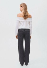 Vit off-shoulder blus i texturerat tyg med volangkant, ihop med högmidjade, löst sittande mörkgrå jeans.
