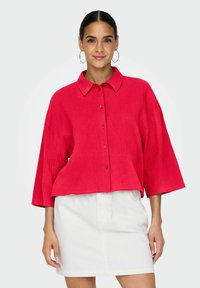 Camicia rossa brillante a maniche corte, con bottoni e tessuto texturizzato, dal taglio morbido. Presenta un colletto classico e bottoni frontali.