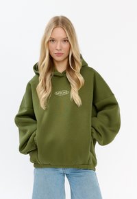 Olivegrüner übergroßer Kapuzenpullover mit einer Zugkordelkapuze, gerippten Bündchen und Saum. Mit dem Logo "MIRONS" in kontrastierendem weißen Stickerei.