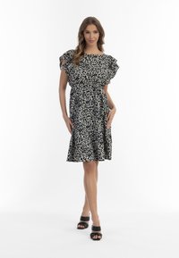 Kleid mit Leopardenmuster, kurzen Rüschenärmeln, tailliert und mit einem ausgestellten Rock. In Schwarz und Cremefarben. Getragen mit schwarzen Blockabsatzsandalen.