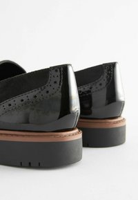 Scarpe in pelle verniciata nera con superficie testurizzata, dettagli a punta d'ala, una soletta marrone e una suola in gomma nera con battistrada.