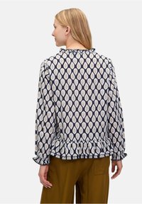 Bluzka w wzory z granatowym tłem, kremowymi i złotymi motywami w kształcie kropli, długimi rękawami, falbaniastym dekoltem oraz peplum. Miękka faktura materiału.
