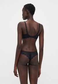 Ensemble de lingerie en dentelle noire avec un délicat bord festonné et une texture transparente, bretelles ajustables sur le soutien-gorge et un string assorti.