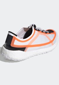 Sneaker con tomaia in rete bianca con accenti arancioni e neri, suola bianca imbottita e supporto per il tallone nero per la stabilità.