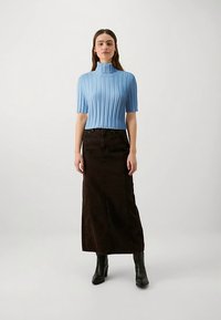 Světlomodrý žebrovaný krátký rukáv s rolákem, kombinovaný s dlouhou tmavě hnědou džínovou sukní. Modelka má na nohou černé kotníkové boty na podpatku.