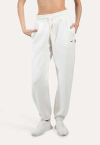 Weiße Jogginghose aus weichem Stoff mit schmal zulaufendem Bein, elastischem Bund, Kordelzug und Taschen, mit einem kleinen Logodetail.