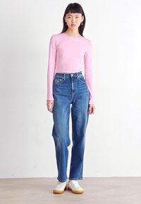 Langærmet lyserød ribbet top, parret med højtaljede blå denimjeans, der har en afslappet pasform, og hvide sneakers med en beige sål.