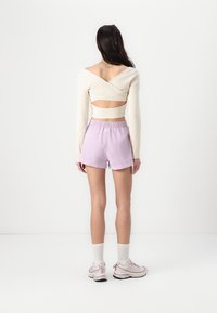 Off-white langærmet top med indviklet design og udsnit i ryggen, parret med lyse lilla shorts og hvide ankelstrømper. Lyse sneakers fuldender looket.