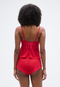 Camisole en satin rouge à fines bretelles et design en couches, associée à un short assorti avec un ourlet incurvé. Texture lisse, style minimaliste.