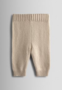Pantaloni beige per neonati lavorati a maglia con vita e polsini a coste, mostrati distesi su uno sfondo grigio chiaro.