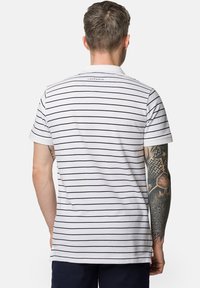 Pasiasta koszulka polo w bieli i granacie, wykonana z bawełny, z krótkimi rękawami i kołnierzykiem. Posiada znakowaną metkę na plecach i widoczne tatuaże na ramionach.