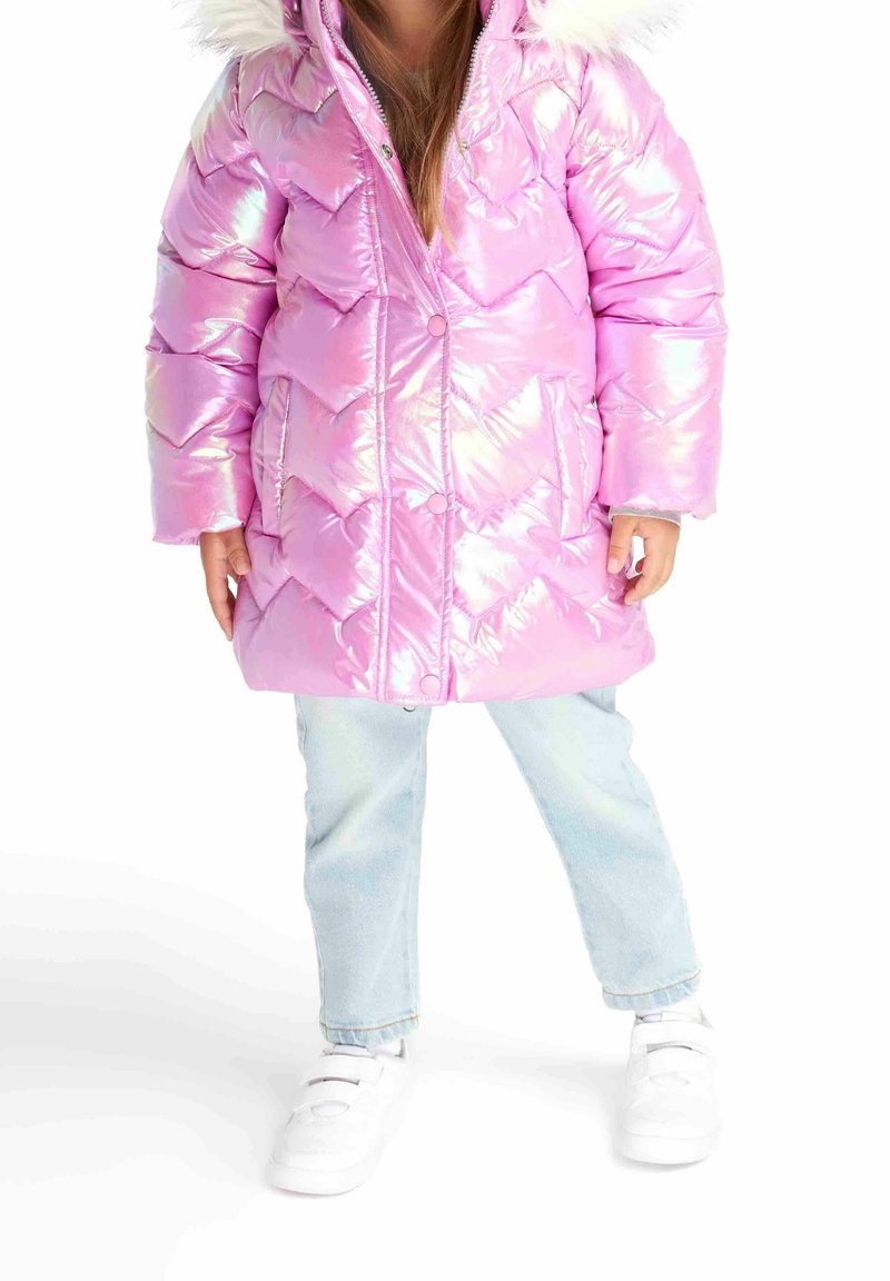 Enfant portant un manteau matelassé rose brillant avec une capuche bordée de fourrure, un jean bleu clair et des baskets blanches, debout sur un fond blanc.