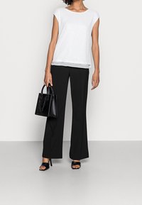 Top blanco con lentejuelas y mangas cortas, combinado con pantalones anchos negros. Lleva un pequeño bolso negro con detalles de cadena. Sandalias negras de tacón.