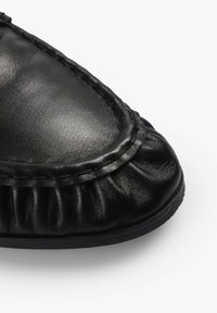 Zapato de cuero negro con punta redonda, textura plisada en el borde y detalle de costura en contraste a lo largo de la costura.