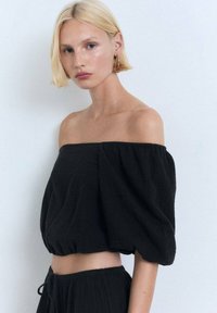 Haut noir sans épaule avec des manches bouffantes et un ourlet court. Fabriqué en tissu texturé avec une coupe décontractée, assorti à un bas coordonné.