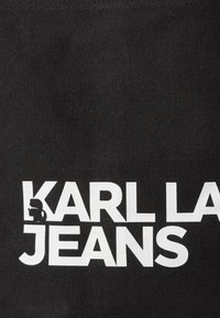 Tessuto nero con la scritta "KARL LAGERFELD JEANS" in grassetto bianco, accompagnata da un piccolo logo a silhouette sulla sinistra.