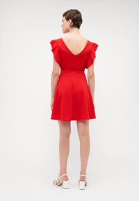 Robe rouge évasée avec des manches courtes à volants, dos en V profond et taille cintrée. Fabriquée en tissu lisse, présentant une couleur unie sans motifs.