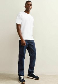 Camiseta de algodón blanca, jeans de mezclilla azul oscuro y zapatillas negras con cordones blancos. Corte recto y diseño sencillo.