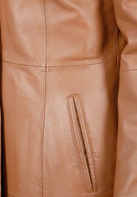 Braune Lederjacke mit einem sichtbaren vertikalen Taschenbereich. Das Material ist glatt mit feiner Körnung und ordentlich genähten Nähten.