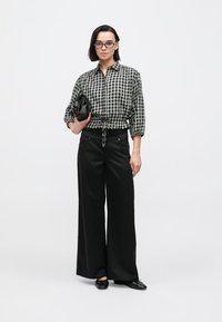 Black and white checkered button-up shirt with a tied waist, paired with wide-leg black trousers and a small black handbag.