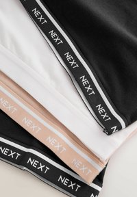 Pile de bandes de tissu noires, blanches, beiges et noires avec le texte "NEXT" répété le long des bords élastiques.