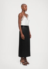 Witte zijden top met kantafwerking, gecombineerd met een zwarte satijnen lange rok en zwarte strap heels. Elegante silhouet met een soepele textuur.