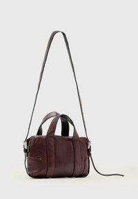 Bordeauxrød læderhåndtaske med to øverste håndtag og en aftagelig sort skulderrem. Har lynlåslukning og en glat, struktureret overflade.