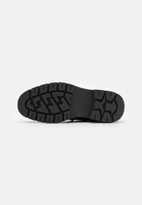 Black rubber shoe sole featuring deep, textured tread patterns for enhanced grip and stability. Smooth finish along the edge.