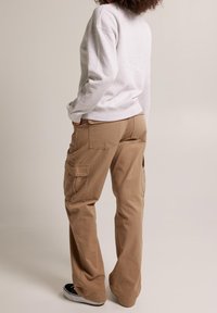 Pantalones cargo beige con múltiples bolsillos laterales, un ajuste holgado y una textura suave, combinados con un suéter de cuello redondo gris claro.