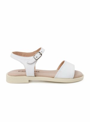 White sandal with a flat sole, adjustable ankle strap, and open toe. Features stitched detailing and a smooth leather-like texture.
