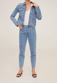 Veste en denim bleu clair à coupe courte, associée à un jean bleu clair à taille haute. Présente des poches classiques et des boutons argentés.