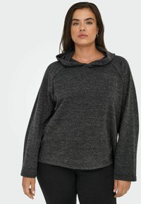 Siv hoodie z teksturo, s kapuco in dolgimi raglan rokavi. Rob je rahlo okrogel, kar nudi sproščen fit. Obuten je z črnimi hlačami.