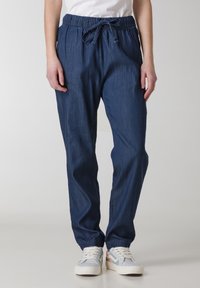 Dunkelblaue Denim-Jogginghosen mit einem elastischen Taillenbund, verstellbarem Kordelzug und elastischen Bündchen, kombiniert mit weißen und pastellfarbenen Sneakern.