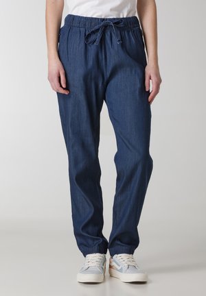 Joggers in denim blu scuro con una vita elasticizzata, cordino regolabile e polsini elastici, abbinati a sneakers bianche e pastello.