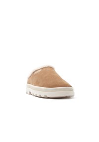 Beige mockask slip-on sko med vit faux fur krage och en strukturerad, flexibel gummisula med ett texturerat mönster.