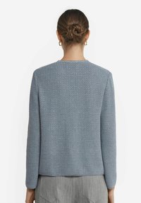 Hellblau strukturierte Jacke mit langen Ärmeln und rundem Ausschnitt. Mit einem gewebten Muster und leicht verkürztem Saum gestaltet.