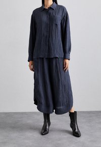 Navy crinkled button-up shirt with a single chest pocket, paired with a flowing navy maxi skirt and black ankle boots.