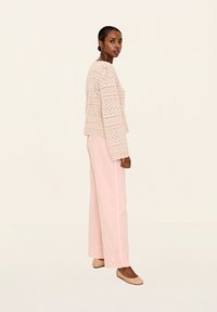 Helles rosa gestricktes Oberteil mit geometrischen Mustern, kombiniert mit locker sitzenden hellrosa Hosen und nackten Schuhen ohne Absatz. Einfaches, strukturiertes Design.