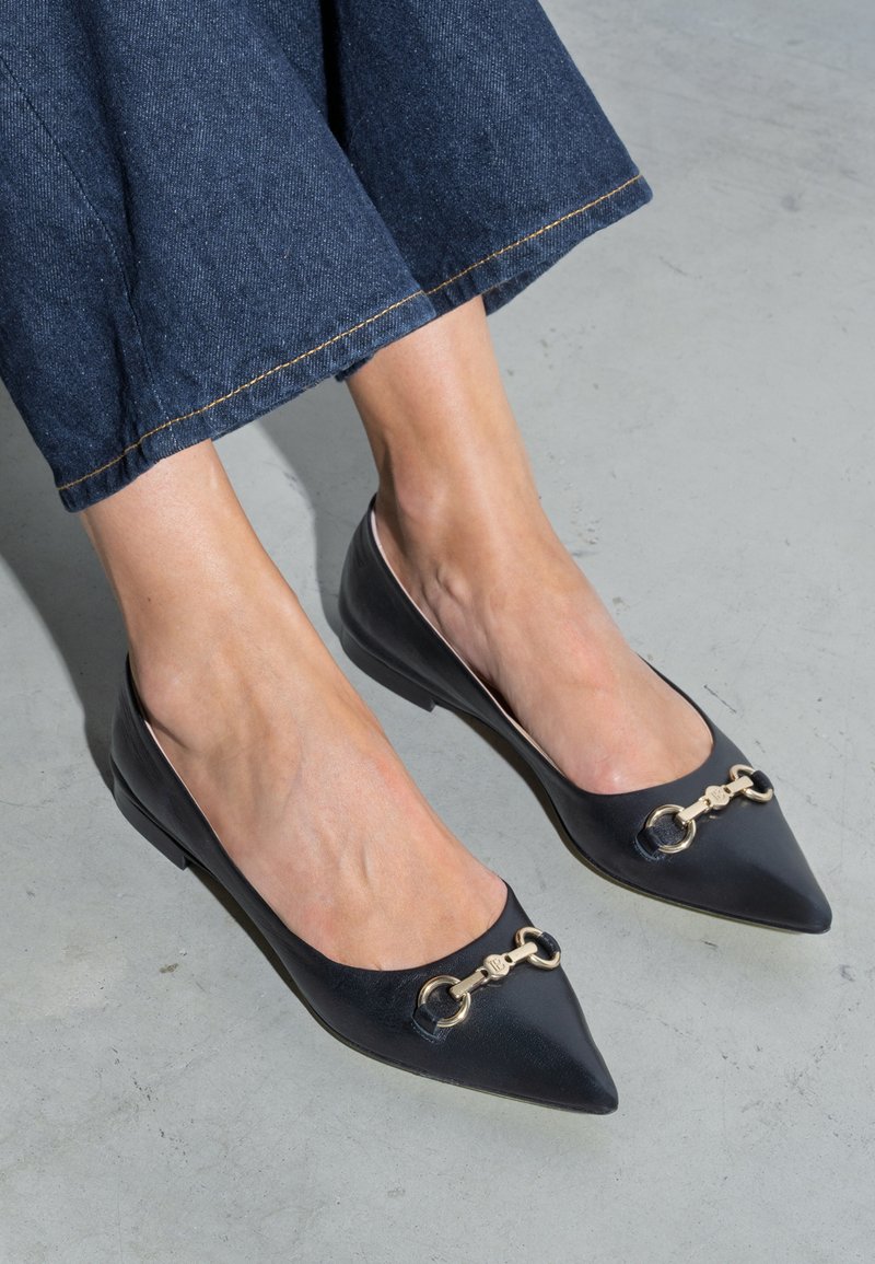 Zwarte leren ballerina's met puntige neuzen, voorzien van gouden kettingaccenten aan de voorkant en een strak, minimalistisch ontwerp. Gemaakt om te dragen met donkere denim.