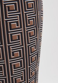 Leggings, jotka esittävät mustista, ruskeista ja valkoisista muodoista koostuvaa geometristä kuviota. Valmistettu joustavasta materiaalista, jossa on sileä rakenne.