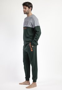 Conjunto de loungewear en verde y gris que incluye una camiseta de manga larga con un diseño de bloques de color y texto impreso, acompañado de pantalones cónicos a juego.